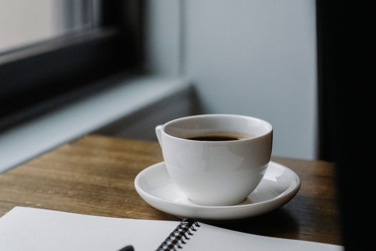 A cup of coffee beside an open notebook and pen